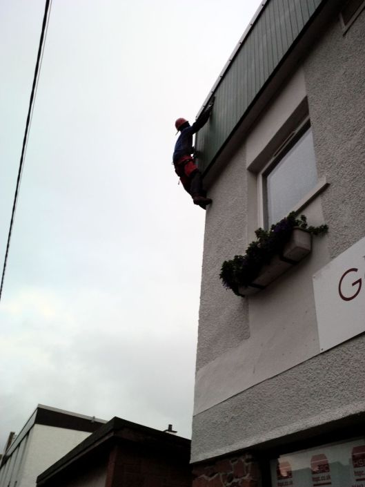 The intrepid climber is on the wall of the Outdoor Shop in Ullapool